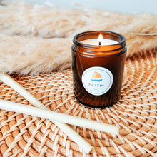 Load image into Gallery viewer, Lit Islands candle on rattan tray with lemongrass sticks in foreground