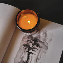 Load image into Gallery viewer, Lit candle sitting on a book with a tree picture 
