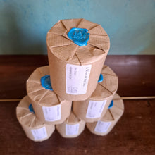 Load image into Gallery viewer, Stack of brown papered candles with blue sealing stamps on a wooden surface.
