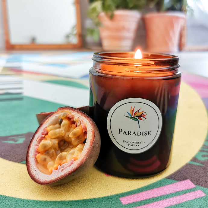 Lit Paradise candle on a colourful mat, with a cut passionfruit leaning against it